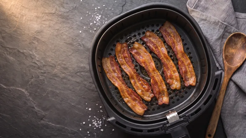 Illustrative photo of streaky bacon rashers in a black air fryer basket