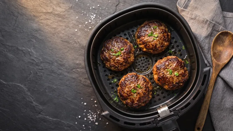 Illustrative photo of beef burger patties in a black air fryer basket