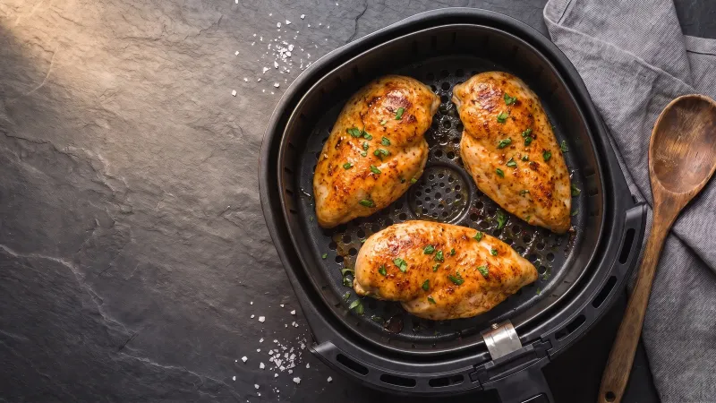 Illustrative photo of three golden chicken breasts in a black air fryer basket