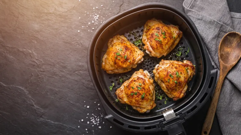 Illustrative photo of golden chicken thighs in a black air fryer basket