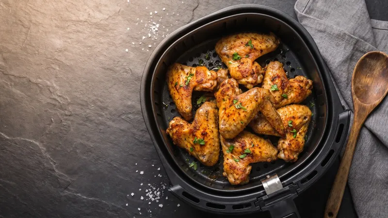 Illustrative photo of golden chicken wings in a black air fryer basket