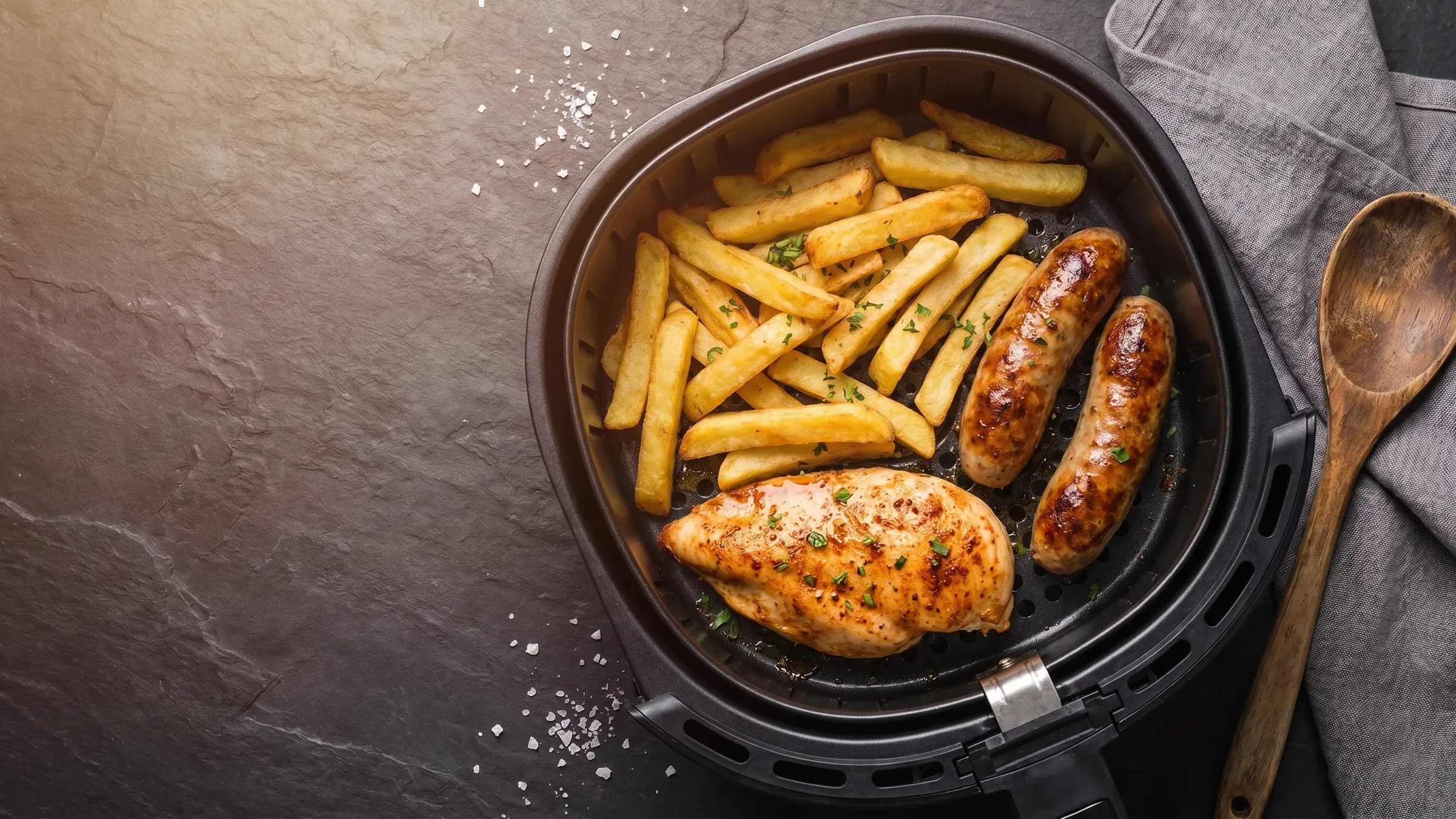 Illustrative photo of golden food in a black air fryer basket on a dark slate surface