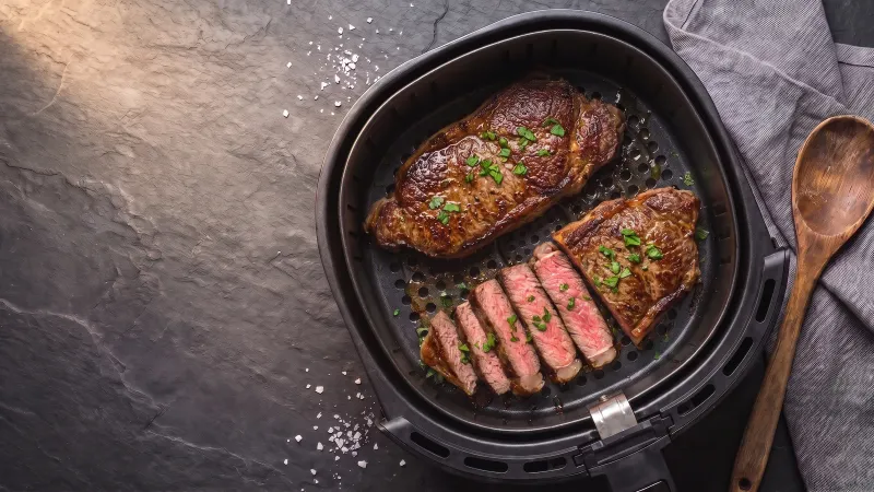 Illustrative photo of two seared sirloin steaks, one sliced to a pink centre, in a black air fryer basket