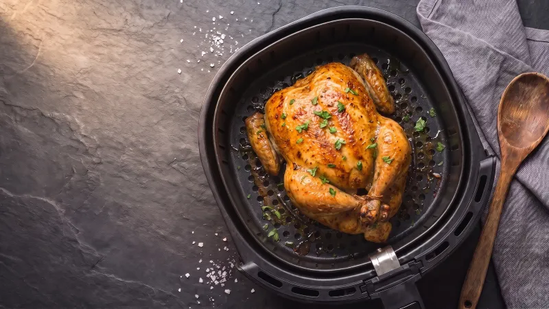 Illustrative photo of a whole roast chicken with golden skin in a black air fryer basket